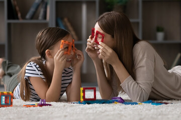 Wall Mural - Happy young Caucasian mother and cute small teenage daughter have fun play together with colorful blocks at home. Smiling mom and little girl child laugh involved in creative playful game activity.