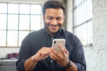 Positive Indian Guy Using Smartphone For Online Communication, Smiling Mixed-race Guy Browsing, Scrolling News Feed, Messaging In Social Media,hindu Man Holds Phone And Enjoying New Mobile Application