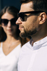 profile of a serious man looking into the distance with glasses on a blurred background of a woman.