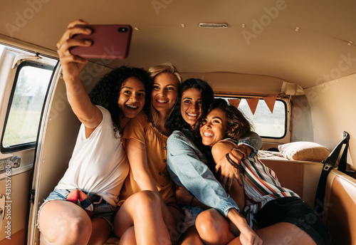 Four beautiful friends taking selfie in a van during a road trip. Smiling women on vacation.