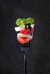 Wall Mural - Caprese salad. mozzarella slices, fresh tomatoes and fresh basil leaves with balsamic sauce on a black fork on a dark background.