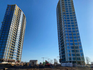 Two tall beautiful modern unfinished new buildings made of glass and concrete against a blue sky