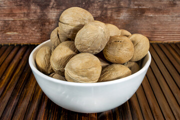 Walnuts in a white bowl on a brown wooden mat.