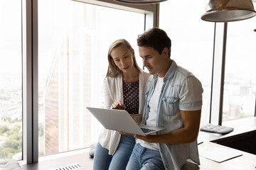 Wall Mural - Young businesspeople gather in modern office look at laptop screen think discuss company project on gadget. Motivated successful employees brainstorm work on computer together. Teamwork concept.