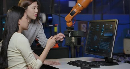 Team of Young Asian Female Industrial Robotics Engineer using Computer to Test and Program Robot Arm at late night in a Research Laboratory. People with technology or innovation concept.