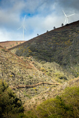 Canvas Print - Landscape of the Serra da Lousã, in Portugal, with the upper part of the Ribeira de Quelhas walkway illuminated by the afternoon sun and at the top of the mountain, 2 wind turbines.