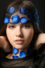 Wall Mural - Beautiful young woman with blue rose petals on dark background