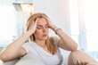 © Graphicroyalty - Portrait of a young blond woman sitting on the couch at home with a headache and migraine . Beautiful woman suffering from chronic daily headaches. Sad woman holding her head because sinus pain