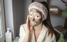 Portrait Of A Young Beautiful Woman In A Dressing Bathrobe And With A Cosmetic Green Mask On Her Face. Concept Of Self Care, Beauty Procedures And The Use Of Natural Cosmetics