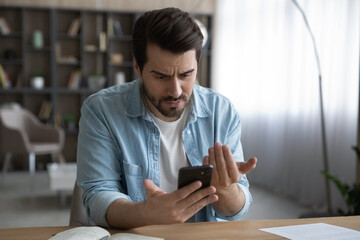 Close up unhappy dissatisfied businessman looking at phone screen, reading bad news in message, confused young male having problem with broken or discharged device, data loss or software failure