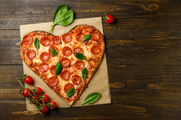 Heart shaped pizza pepperoni on dark wooden background with spinach and tomatoes cherry