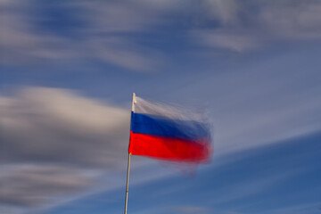 Realistic flag of Russia waving in the wind against deep blue sky.