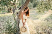 Tender Portrait Of Beautiful Brunette Woman In Beautiful Sunlight. Woman In Yellow Summer Linen Dress In Olive Tree Garden. Natural Beauty.Travel To Italy, Summer Vacation