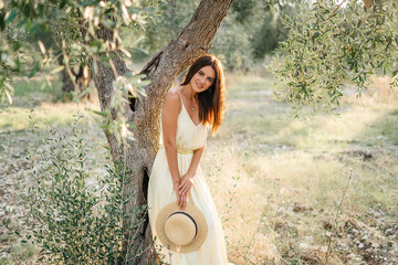 Tender portrait of beautiful brunette woman in beautiful sunlight. Woman in yellow summer linen dress in olive tree garden. Natural beauty.Travel to Italy, summer vacation