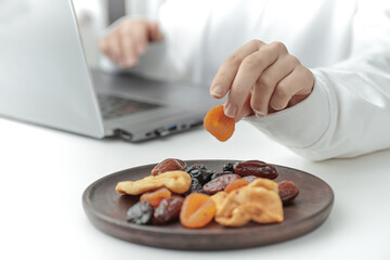 A female taking a dried fruit from a wooden bowl.