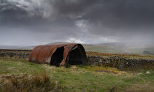 Old Tin Shed In The North Pennine Landscape Near Garrigill, Cumbria With A Snow Shower In The Landscape Behind
