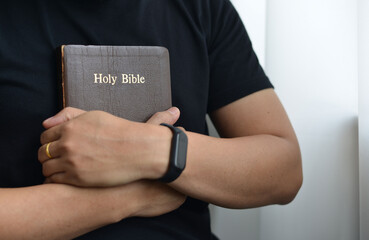 A man is holding and hug the bible in the morning. Hands folded in prayer on a Holy Bible in church concept. worship and religion. copy space