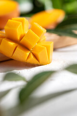 Diced fresh mango fruit on wooden cutting board with sunlight and leaf shadow.