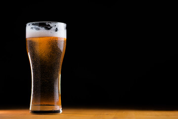 Glass of light beer on a wooden table, black background