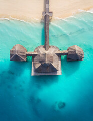 Wall Mural - Aerial shot of the Stilt hut with palm thatch roof washed with turquoise Indian ocean waves on the white sand sandbank beach on Zanzibar island, Tanzania.