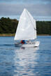 Sailboat of the optimist on the lake with a children's crew on the deck against the backdrop of the forest on a sunny day 