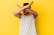 Young tattooed caucasian man isolated on yellow background keeping two arms crossed, denial concept.