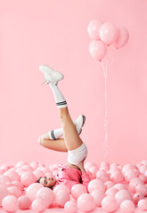 Young pretty woman have fun with legs up lying in pink balloons over pink pastel background