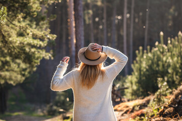 Woman with hat enjoying fresh air and spring sunlight during hike in forest