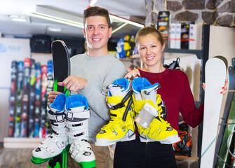 Wall Mural - Happy young customers are demonstrating their choice of ski and boots for skiing in sport shop.