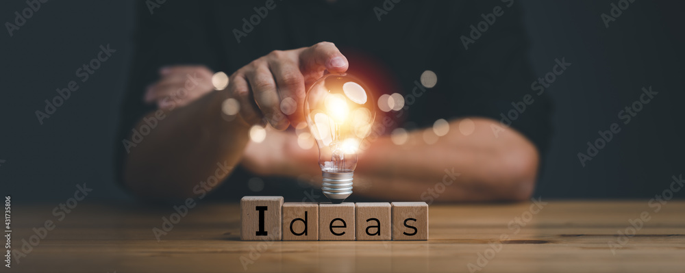 hand touching on light bulb on wood block with Word Ideas, new idea concept with innovation and inspiration, innovative technology in science and communication concept. - obrazy, fototapety, plakaty 