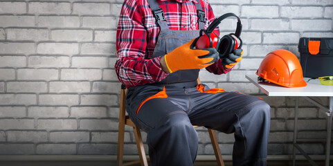 Wall Mural - Man worker in uniform putting protective headphones. Construction safety. Banner.