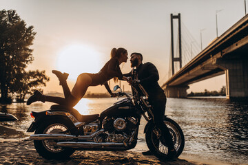 Evening walk of a biker and a girl on the river bank. Photoshoot at sunset.