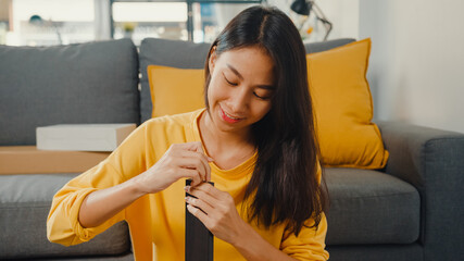 Wall Mural - Happy asian young woman unpacking box and reading the instructions to assemble new furniture decorate house build table with carton box in living room at home.