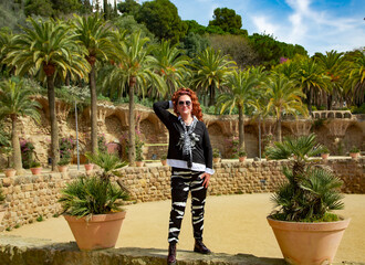 Pretty woman with bright curly hair in a silk black suit against the backdrop of a beautiful palm garden. Enjoying a bright summer day in a green park.