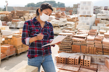 Woman manager in protective mask leads the accounting of materials at the construction site