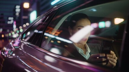 Wall Mural - Beautiful Businesswoman is Commuting from Office in a Backseat of Her Car at Night. Entrepreneur Using Smartphone while in Transfer Taxi in Urban City Street with Working Neon Signs.