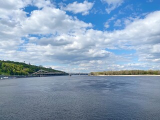 Sticker - Ukraine Kiev city landscape. Dnieper river calm blue water at summer sunny day. Summertime, tranquility, relax. Scenic natural landscape. Spectacular cloudy sky. Pedestrian bridge over the river. 