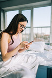 Fototapeta  - Young caucasian woman resting on a bed at home and using laptop computer and smartphone. Chatting with friends, shopping online.