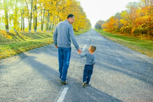 A Happy Parent With Child Are Walking Along The Road In The Park On Nature Travel