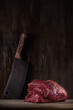 large piece of raw beef tenderloin lezhin on a cutting board with a kitchen cleaver on the background of an old wooden wall. artistic photo with copy space