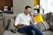 © Dragosh - Portrait of a smiling young man sits on the couch comfortably holding a stationary phone.