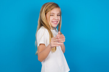 Wall Mural - Hey you, bang. Joyful and charismatic good-looking beautiful Caucasian little girl wearing white T-shirt over blue background winking and pointing with finger pistols at camera happily and cheeky.