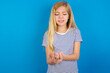 © Roquillo - Caucasian kid girl wearing striped shirt ​against blue wall  Suffering pain on hands and fingers, arthritis inflammation