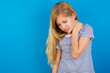 © Roquillo - Caucasian kid girl wearing striped shirt ​against blue wall  Suffering of neck ache injury, touching neck with hand, muscular pain