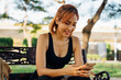 © twinsterphoto - Young Asian fit woman in sportswear sitting on bench checking mobile phone. Asia girl taking a break during morning run in outdoor park