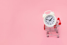 White Alarm Clock Lies In The Shopping Cart On Pink Background. Big Sale Time Concept. Copy Space.