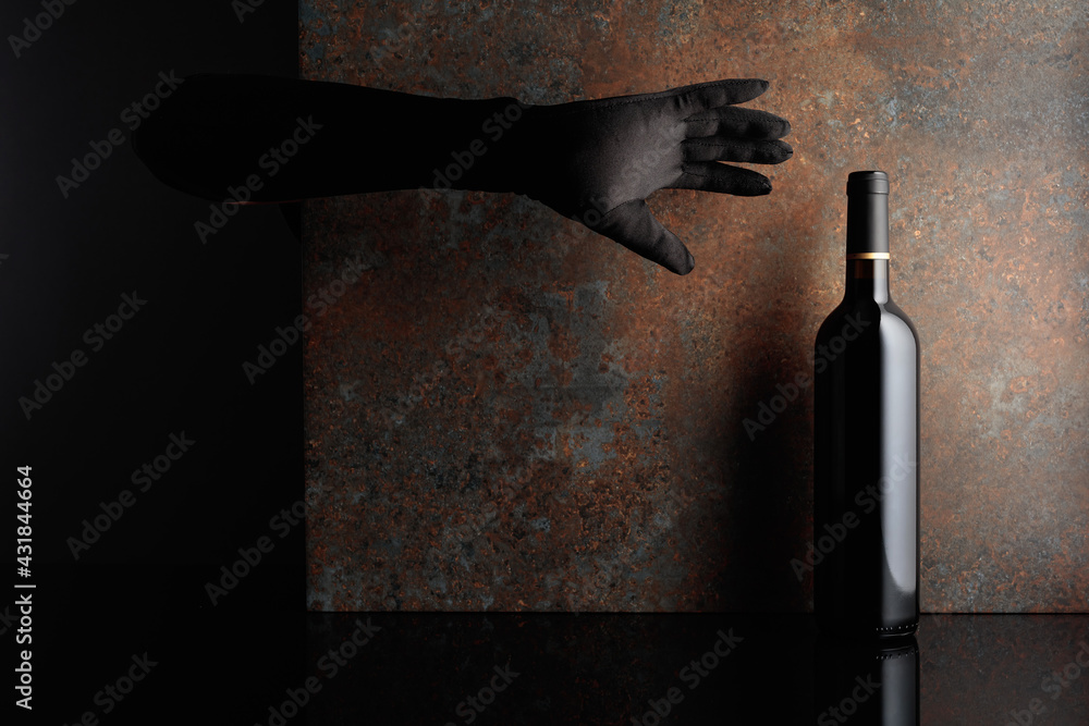 Woman hand in  glove reaches for a bottle of red wine. - obrazy, fototapety, plakaty 