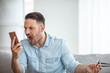 Portrait of angry young man screaming on his mobile phone. Portrait of a furious young businessman yelling at mobile phone. Aggressive man in blue shirt screaming at smartphone