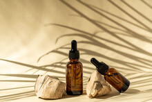 Dark Glass Cosmetic Bottles With A Dropper On A Beige Background With Stones And Tropical Leaves. Natural Cosmetics Concept, Natural Essential Oil And Skin Care Products