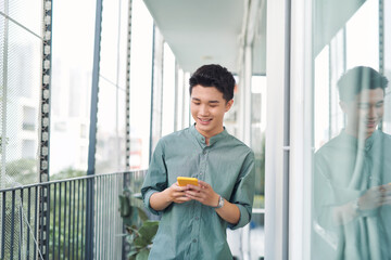 Wall Mural - Young man standing on balcony texting on mobile phone,